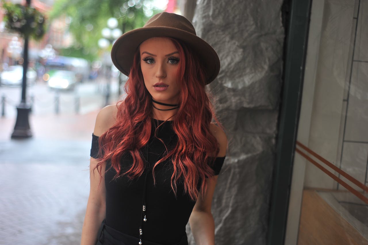 Fashionable woman with red hair posing outdoors wearing a stylish hat.